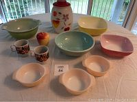 Overview of all ovenware, cookie jar, cups, and apple container on table in daylight with garden view