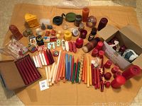 Wide angle photo showing full assortment of candles spread out on fabric cloth surface with many taper candles, shaped and pillar candles, and boxed candles.