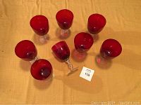 Eight red glass goblets arranged on an orange surface, showing overall condition and design.