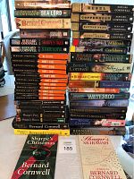 Photo showing a stack of Bernard Cornwell books including multiple titles from the Sharpe series as well as other historical novels, with two illustrated Sharpe-themed booklets in front.