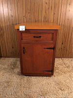 Front view of wooden kitchen island with butcher block top, drawer, and cabinet door.