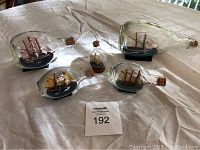 Five ships in bottles arrayed on table showing variety of bottle shapes and ship models
