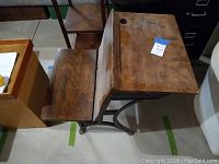 Angle view showing the antique school desk with attached seat, worn wooden surface, and metal legs on a concrete floor.