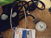 Manual blood pressure cuff with gauge, attached stethoscope, and inflation bulb on wooden surface