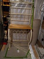 Full view of cream-colored metal baker's rack with wooden shelf and wine bottle slots.