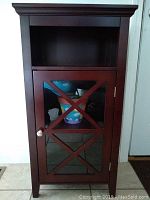 Front view of cherry finish occasional table cabinet with glass door and cross design