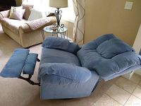 Blue recliner chair shown fully reclined with footrest extended. Chair is upholstered in light blue fabric with padded armrests and cushioned headrest.