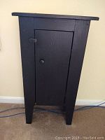 Front view of small black solid wood cabinet with one door and knob.