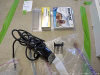 Photo showing black electric pet grooming clippers with cord, clipper comb attachment and two unopened Frontline flea and tick treatment packages for medium dogs.