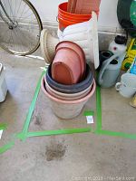 Stack of various plastic planters and buckets including rectangular and oval shapes and orange five-gallon buckets.