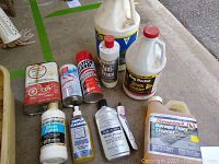 Photo showing various cleaning and polishing bottles and cans, opened with some usage visible, including Thompson's Garage Floor Cleaner, Weiman Metal Polish, and pest spray.