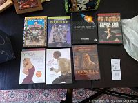 Top down photo of assorted eight DVDs including Jumanji, Beetlejuice, Planet Earth, Thank You for Smoking, Yoga Weight Loss, 13 Years a Slave, Dogville.