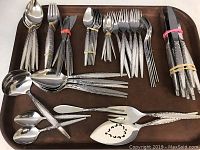 Full view of all flatware items bundled in groups on a wooden tray showing forks, knives, spoons, and serving utensils.