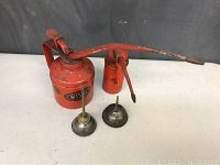 Wide view showing four oil cans: one large red Wesco oil can with a long curved spout and pump handle, one smaller red oil can, and two small metal oil pourers with brass nozzles.