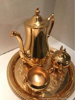 Full tea set on tray showing coffee pot, sugar bowl, creamer, and ornate tray in gold plating with reflective surfaces.