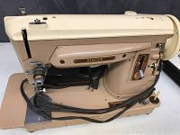 Full side view of the vintage Singer sewing machine showing brown and cream metal body with an attached power cord and foot pedal.