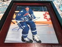 Framed signed photo of hockey player wearing blue uniform number 13 playing on ice rink, signed in blue ink.