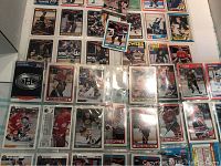 Photo showing numerous hockey cards arranged on a flat surface, including cards from various NHL teams and players in protective sleeves.