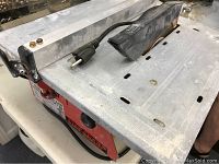 Tile saw showing metal table top, power cord with plug, and rusty blade edge