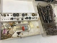 White plastic case open showing various Dremel bits and accessories including grinding wheels, sanding drums, cutting discs, wire brushes, and other small attachments.