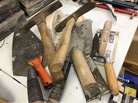 Photo showing multiple masonry tools including trowels and a hammer with wooden handles and metal heads coated in cement residue.