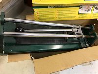 Tile cutter inside original box, showing metal base and chrome rods with handle