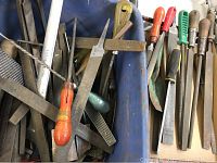 Various metal hand files showing different types such as flat, half-round, round, and triangular with mixed wooden and plastic handles of different colors.