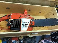 Close-up of the Remington Mighty Mite Bantam orange and black chain saw placed inside the wooden box showing the chain and bar in detail.