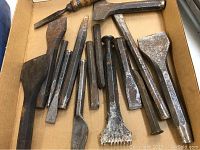 Overview of all chisels and tools in the lot inside a cardboard box, showing rust and wear on all metal parts.
