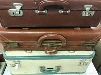 Three vintage suitcases stacked horizontally, showing different colors and handles