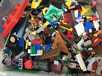 Photo showing a large pile of assorted LEGO bricks, wheels, flat panels, and miscellaneous parts in various colors including red, blue, yellow, green, black, gray, and white.