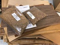 Various wood veneer sheets beneath two bags of granular hide glue on top, showing wood patterns