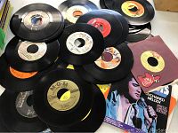 Pile of assorted 45 RPM vinyl records including some in paper sleeves, showing various label designs and colors.
