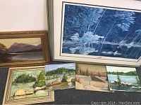 Six paintings and prints leaning against wall on carpeted floor