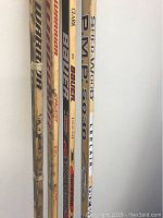 Close-up view of six wooden hockey and goalie sticks showing branding and model names such as Clark, Bauer, Leclaire PMP 5030, SuperWood, Warrior, Sherwood.