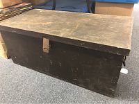 Front and top view of old wooden trunk showing metal latch and worn dark finish.
