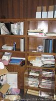 Wooden cabinet shelves containing binders, papers, and craft materials scattered in stacks and containers.