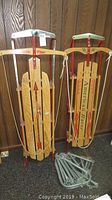 Two vintage wooden sleds standing against a wood-paneled wall, showing Flexible Flyer and American Racer sleds side-by-side.