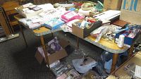 Wide shot of tables covered with assorted quilting fabrics, quilting hoops, and sewing notions including boxes and bags with supplies underneath.