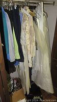 Closet with vintage white and cream wedding gowns and various clothes hanging on hangers.