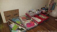 Plastic bins arranged on the floor containing gift wrapping supplies including paper, bags, and tissue paper.
