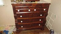 Front view of antique wooden dresser showing five drawers with white porcelain knobs and curved front design.