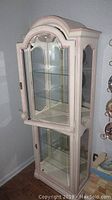 Full view of the curio cabinet showing two glass doors, arched top, and wood frame with distressed finish.