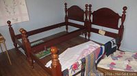 Two assembled single cherry wood poster beds with cannonball finials on posts, minor scratches visible.