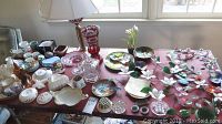 Wide shot of all lot items on table including china, glassware, lamp, figurines, and decorative plates.