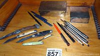 Wide shot showing all items in lot including pocketknives, pens and lidded boxes on wooden surface