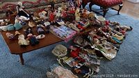 Wide view showing numerous dolls, clothes, and small animals spread across a table and floor area