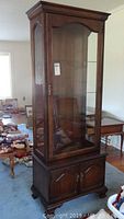 Full view of tall wood curio cabinet with glass door and shelves inside