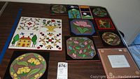 Full view of all 11 art tiles arranged on table including largest 4-tile cluster with house and floral motifs.