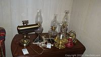 Photo showing three electrified oil lamps with glass chimneys and a bronze desk lamp with cylindrical light fixture.
